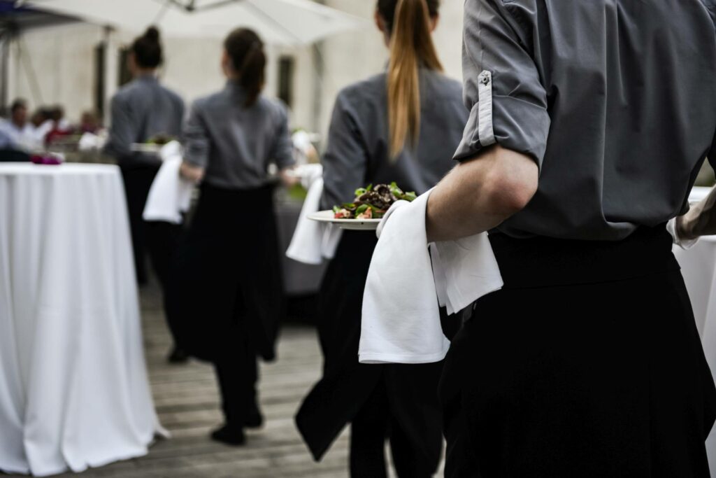 Servicepersonal die hochwertiges Essen auf einer Hochzeit servieren. Sie sind in Grau und Schwarztönen gekleidet