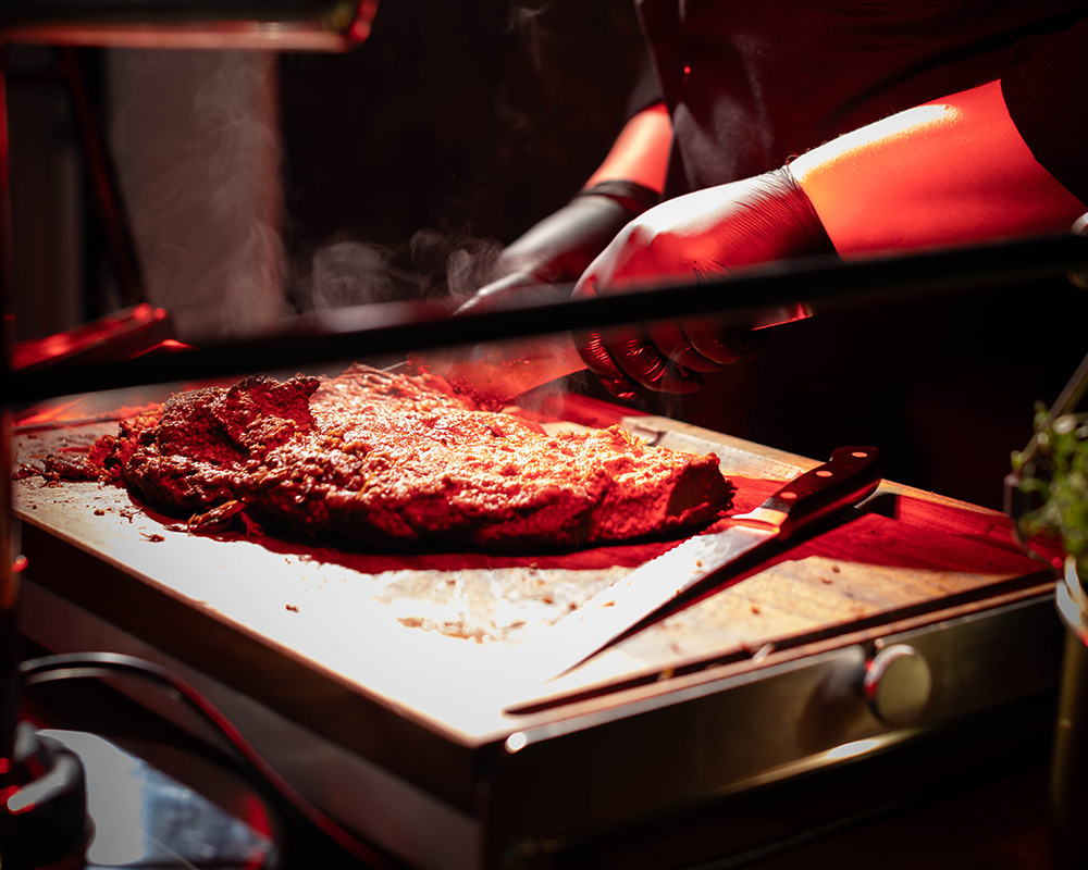 Ein großes, gegrilltes Stück Fleisch wird vom Koch geschnitten.