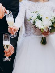Hochzeitspaar und Gäste denen Champagner eingeschenkt wird. Die Braut und zwei andere Gäste halten Blumensträuße in der Hand